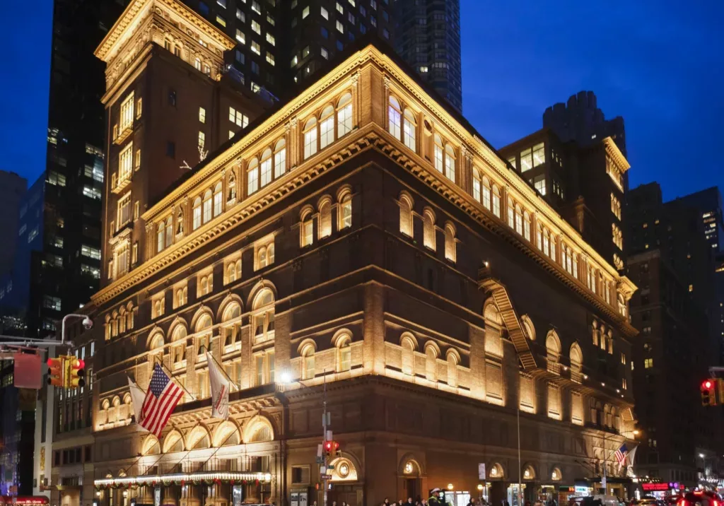 New York, New York, USA - December 11, 2015: Carnegie Hall in Manhattan in the evening. Located on the corner of 57th St. and 7th Ave., Carnegie Hall is one of the most well known concert halls in the world. People and vehicles can be seen.